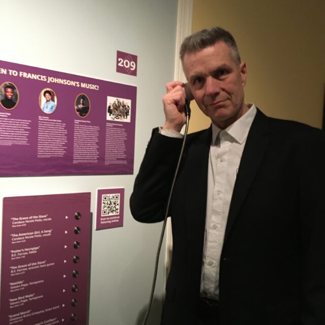 Edward Malouf, Principal of Content•Design Collaborative listening to the Francis Johnson audio interactive at the Black Founder: The Forten Family of Philadelphia at the Museum of the American Revolution.